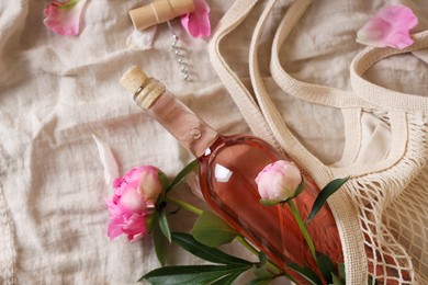 Photo of Flat lay composition with rose wine, mesh bag and beautiful peonies on white fabric