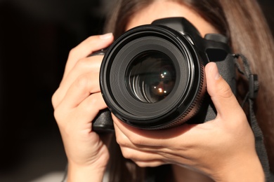 Female photographer with professional camera on dark background, closeup