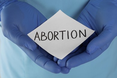 Doctor holding paper card with word ABORTION, closeup