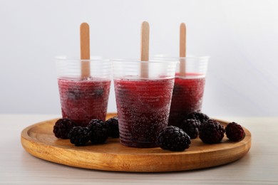 Tasty blackberry ice pops in plastic cups on white wooden table. Fruit popsicle
