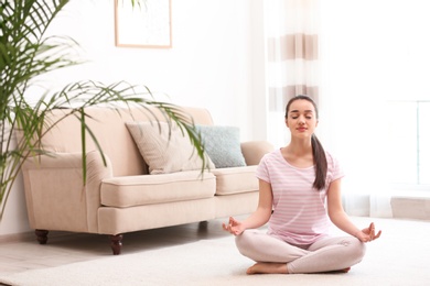 Young woman meditating on floor in living room, space for text. Zen concept