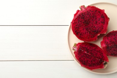 Plate with delicious cut red pitahaya fruit on white wooden table, top view. Space for text