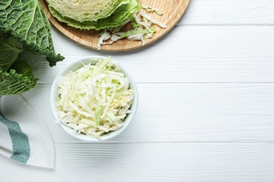 Photo of Cut fresh savoy cabbage in bowl on white wooden table, flat lay. Space for text