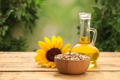 Sunflower, jug of oil and seeds on wooden table against blurred background