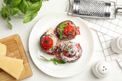 Baked eggplant with tomatoes, cheese and basil served on white wooden table, flat lay