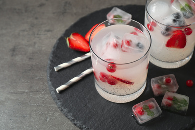 Glasses of refreshing drink with ice cubes and berries on grey table, closeup