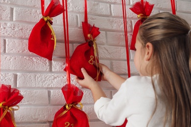 Little girl taking gift from Christmas advent calendar indoors, closeup