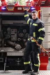 Portrait of firefighter in uniform with entry tool near fire truck outdoors