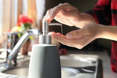 Woman using liquid soap dispenser in kitchen, closeup
