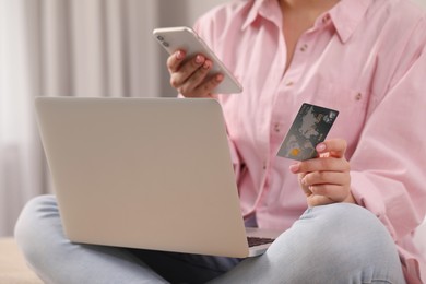 Woman with credit card using laptop and smartphone for online shopping indoors, closeup