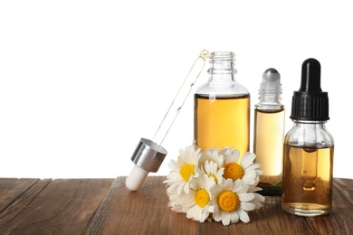 Chamomile flowers and cosmetic bottles of essential oil on wooden table against white background. Space for text