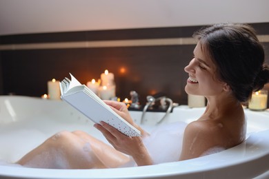 Young woman reading book while taking bubble bath. Romantic atmosphere