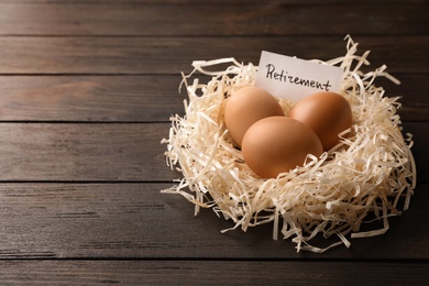 Eggs and card with word RETIREMENT in nest on wooden background, space for text. Pension concept