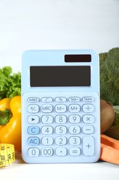 Calculator and food products on white wooden table. Weight loss concept