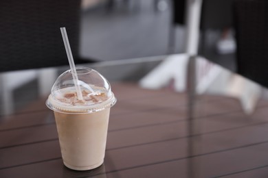 Plastic takeaway cup of delicious iced coffee on table in outdoor cafe, space for text