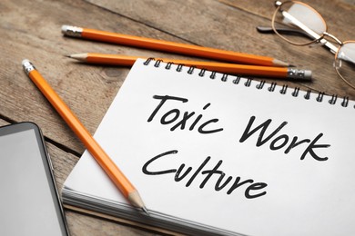 Image of Notebook with text Toxic Work Culture on wooden table, closeup