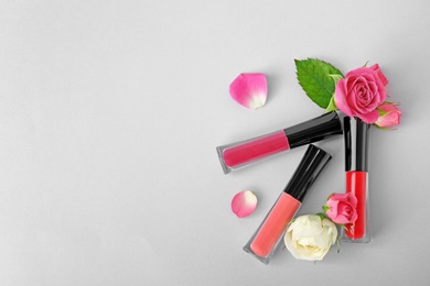 Lip glosses and flowers on light background