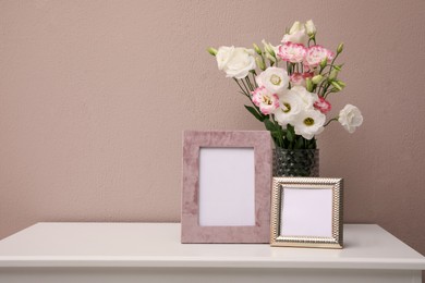 Empty photo frames and beautiful bouquet on white table near pink wall, space for text