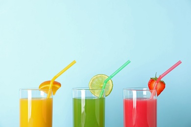 Three glasses with different juices and straws on color background
