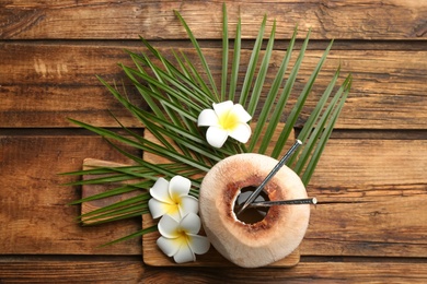 Fresh coconut with drinking straws and flowers on wooden table, flat lay