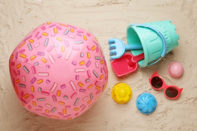 Pink inflatable ball, sunglasses and plastic beach toys on sand, flat lay