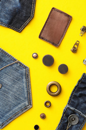 Flat lay composition with garment accessories and cutting details for jeans on yellow background