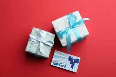 Gift card and presents on red background, flat lay