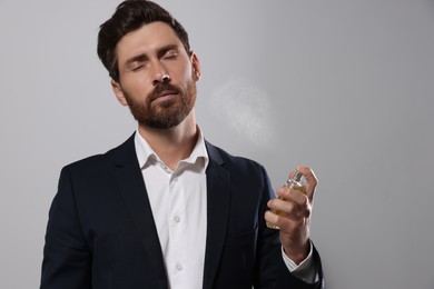 Handsome bearded man applying perfume on light grey background. Space for text