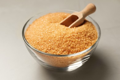 Brown sugar and scoop in glass bowl on light grey table, closeup