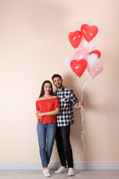 Happy young couple with heart shaped balloons near beige wall. Valentine's day celebration