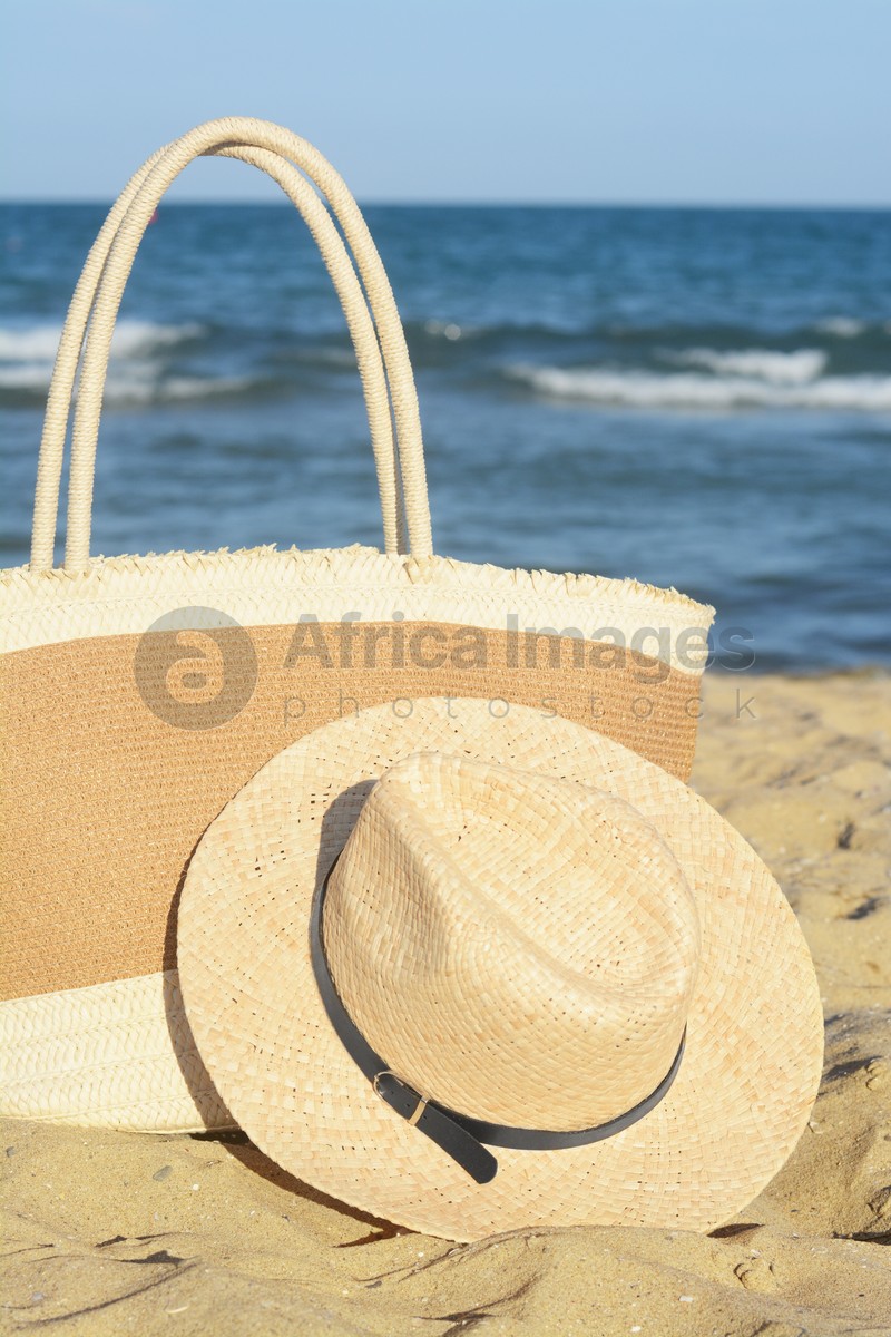 Photo of Stylish bag and hat near sea on sunny day. Beach accessories