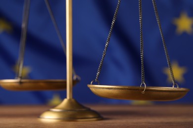 Scales of justice on wooden table against European Union flag, closeup