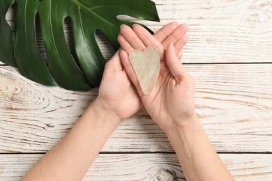 Photo of Woman holding gua sha tool over white wooden table, top view