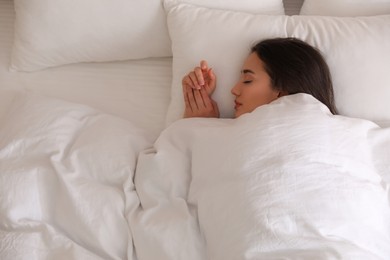 Young woman covered with warm white blanket sleeping in bed, top view. Space for text