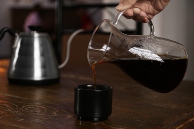Barista pouring coffee into cup at wooden table in cafe, closeup