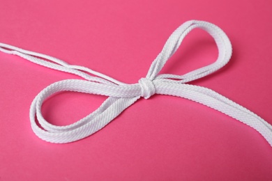 White shoe laces tied in bow on pink background