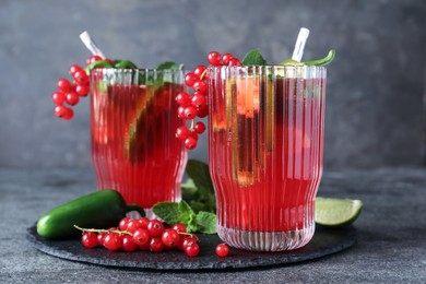 Photo of Glasses of spicy red currant cocktail with jalapeno and mint on grey table