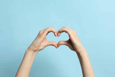 Woman making heart with her hands on light blue background, closeup