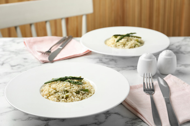 Photo of Delicious risotto with asparagus served on marble table