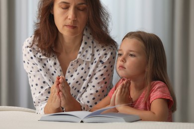 Mature woman with her little granddaughter praying together over Bible in bedroom