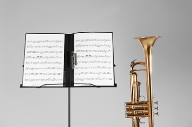 Trumpet and note stand with music sheets on grey background