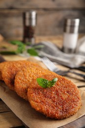 Delicious fried breaded cutlets with basil on wooden table