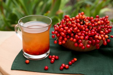 Photo of Cup of tea and fresh ripe viburnum berries on table outdoors