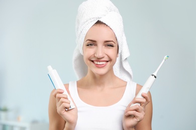 Portrait of young woman with electric toothbrush and paste on blurred background