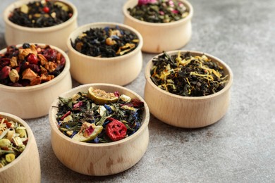 Photo of Different kinds of dry herbal tea in wooden bowls on light grey table