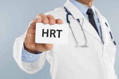 Doctor holding card with abbreviation HRT on light grey background, closeup. Hormone Replacement Therapy