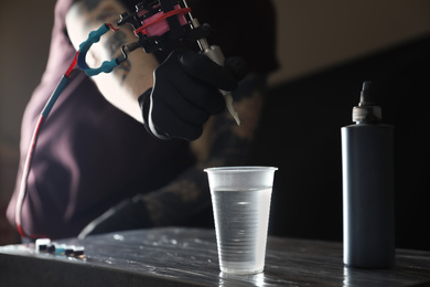 Photo of Tattoo artist cleaning machine needle at table, closeup