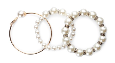 Different elegant bracelets with pearls on white background, top view