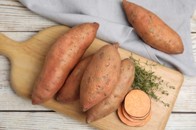 Wooden board with thyme and sweet potatoes on white table, flat lay
