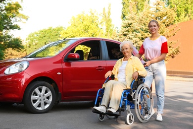Senior woman in wheelchair with granddaughter near car outdoors